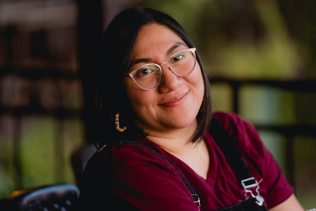 Portrait of a Salvadoran Woman in El Salvador. Shot at sunset on a mountain with soft lighting. She is wearing glasses and smiling into the camera.